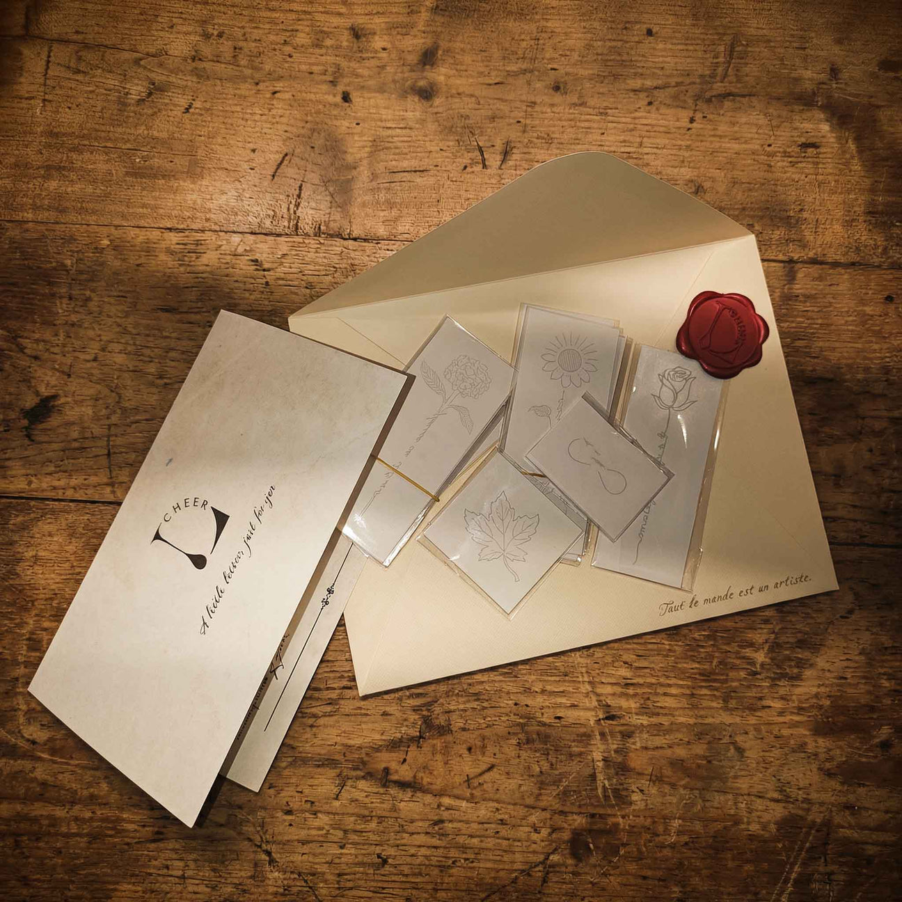 Minimal packaging for semi-permanent tattoos displayed on a rustic wooden table, featuring tattoo sheets, branded envelope packaging, and a wax seal for a natural, artistic aesthetic.