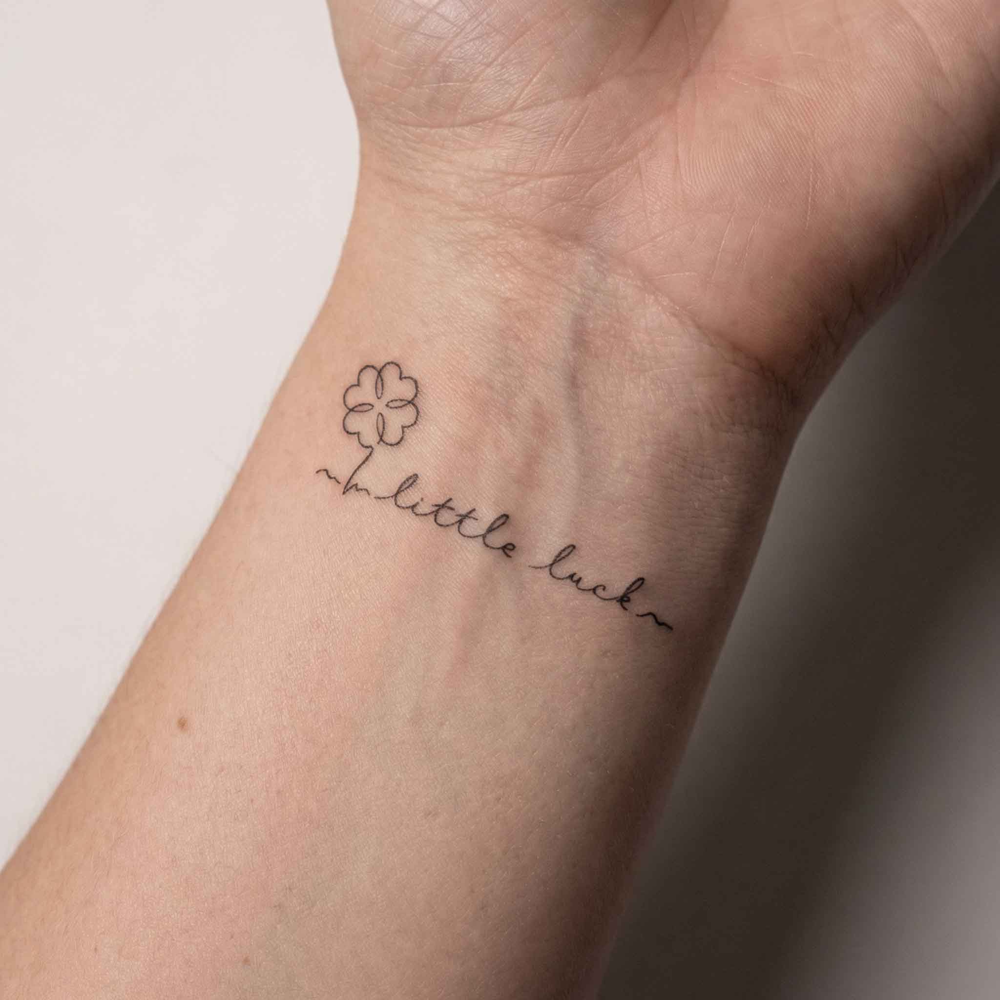 Tiny floral quote tattoos worn on wrist with fine line handwritten style