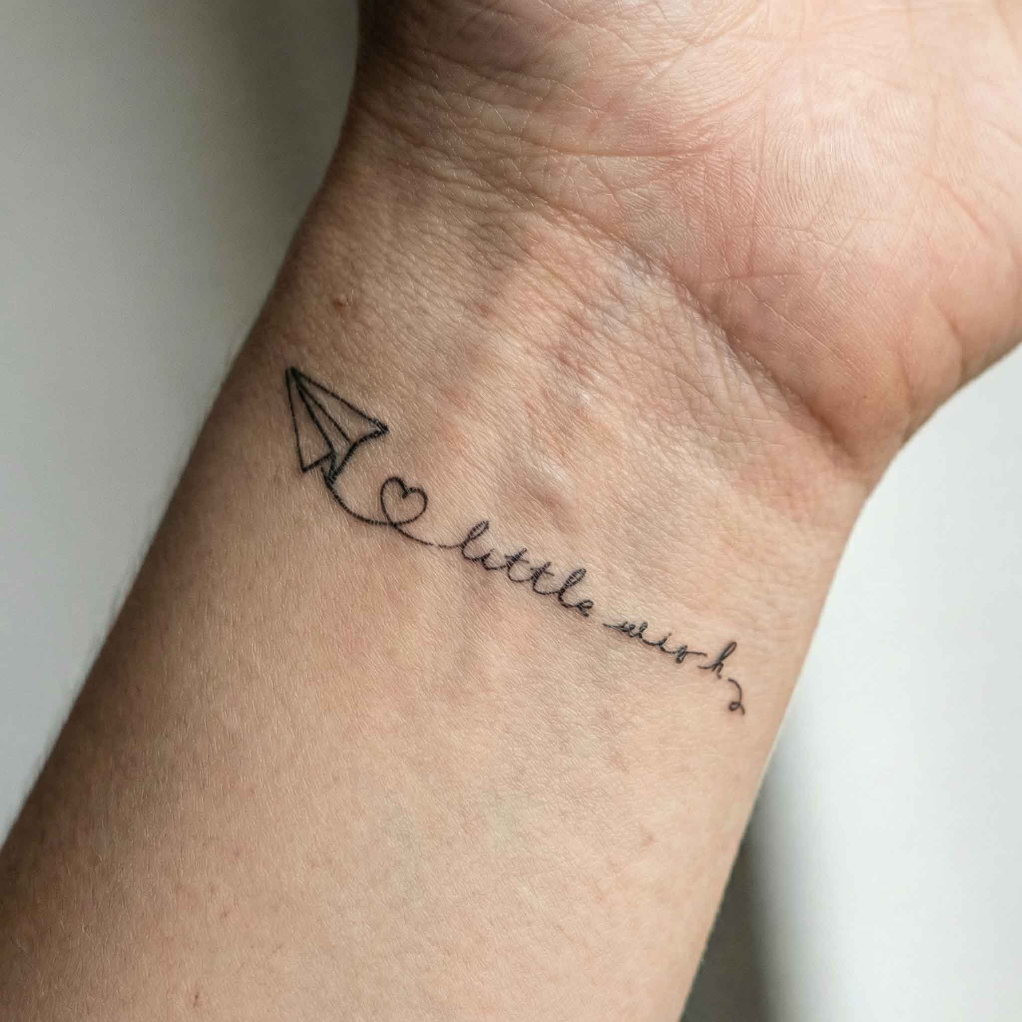 Mini Series paper airplane and word temporary tattoo shown on skin.