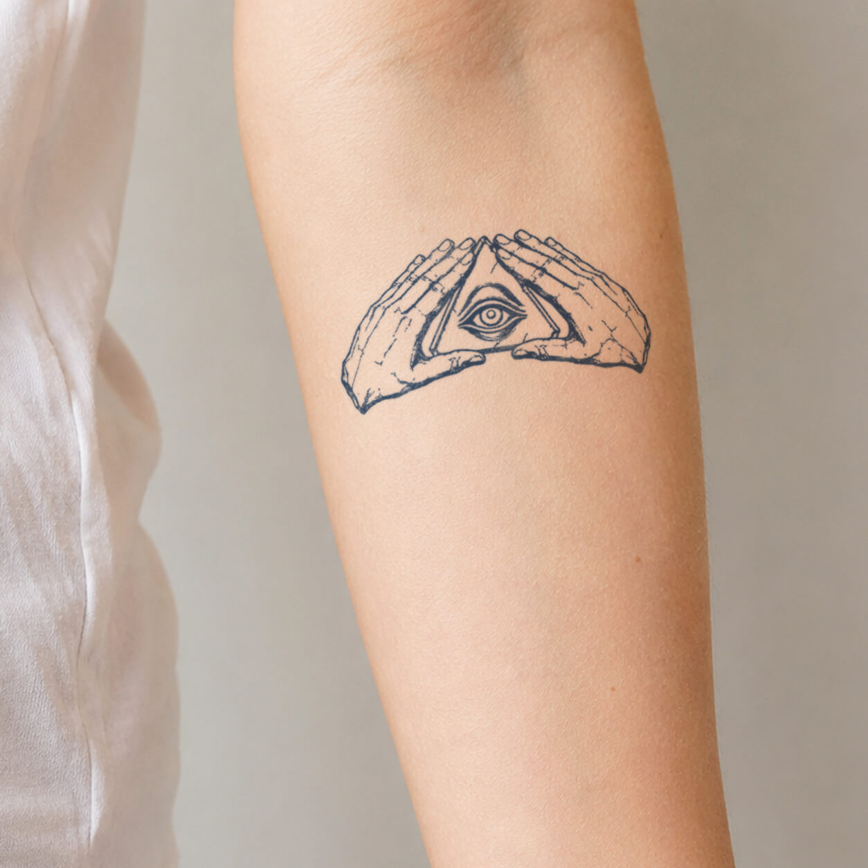 Detailed line art tattoo featuring hands forming a triangle around an all-seeing eye symbol. This mystical temporary tattoo design combines geometric elements, hand illustrations, and symbolic artwork for a bold spiritual-inspired look.
