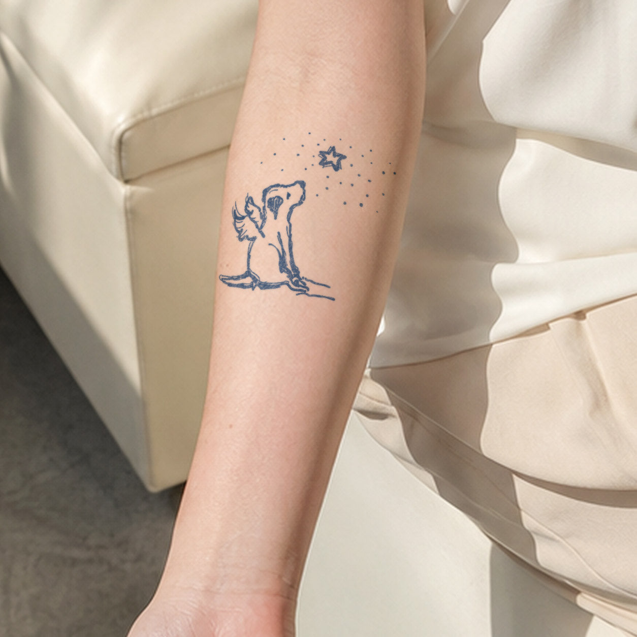 Temporary forearm tattoos featuring a small dog with a single feathered wing looking up toward a starry sky.
