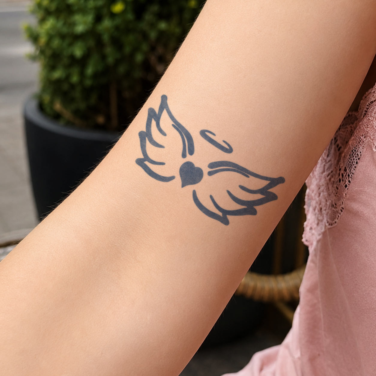 Temporary arm tattoos featuring two feathered angel wings, a solid heart, and a small halo on the forearm.