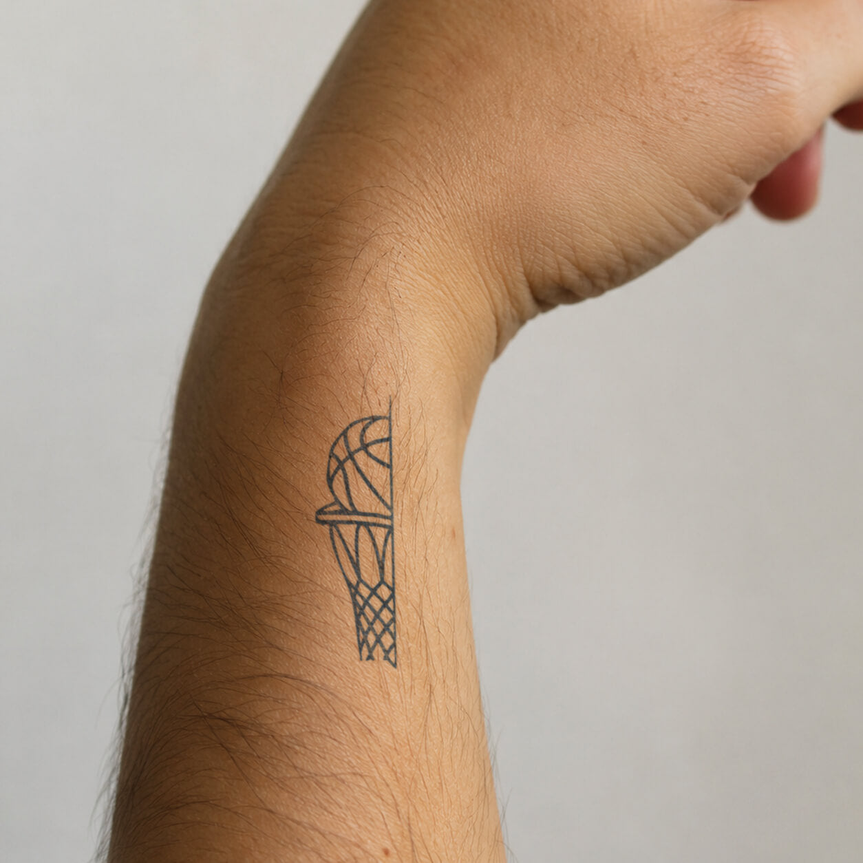 Fine-line basketball hoop and ball design from adult temporary tattoos, placed on the inner forearm for a clean sporty look.