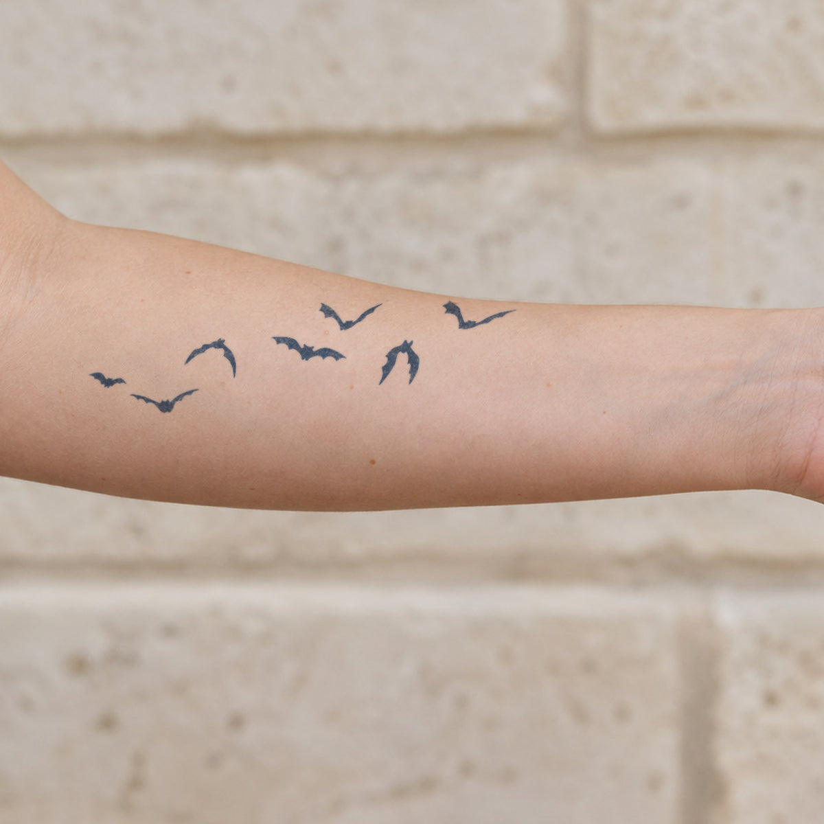 Small temporary tattoos featuring a flock of flying bat silhouettes in blue-black ink across the forearm.