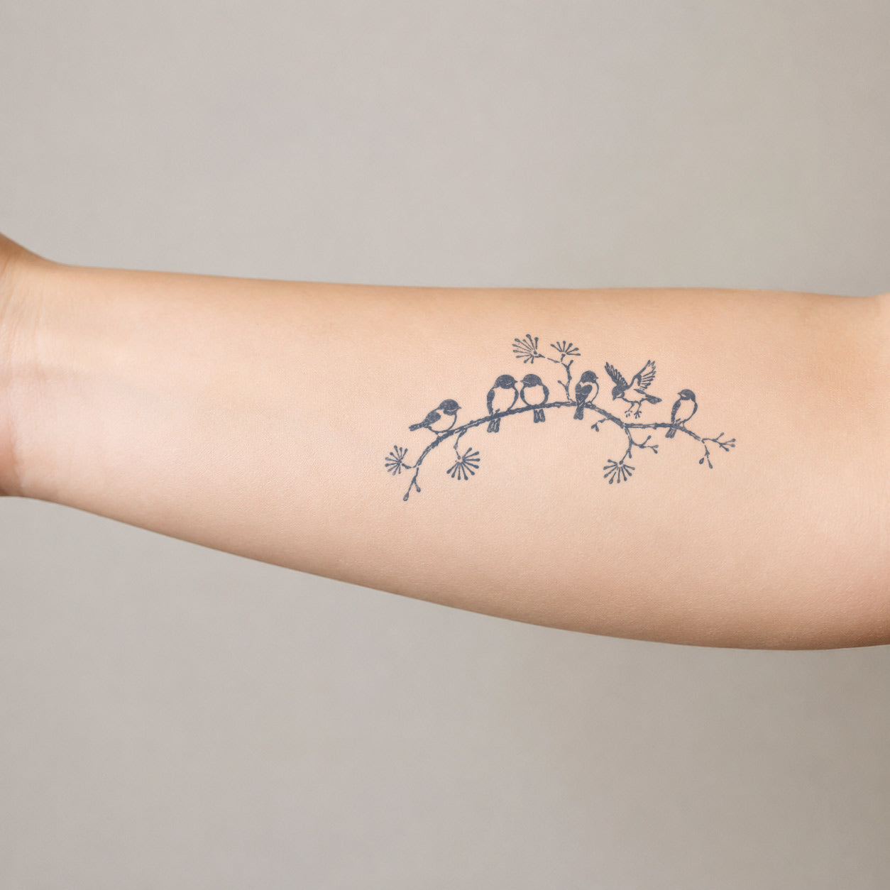 Semi-permanent tattoo featuring small birds resting on a delicate flowering branch across the inner forearm.