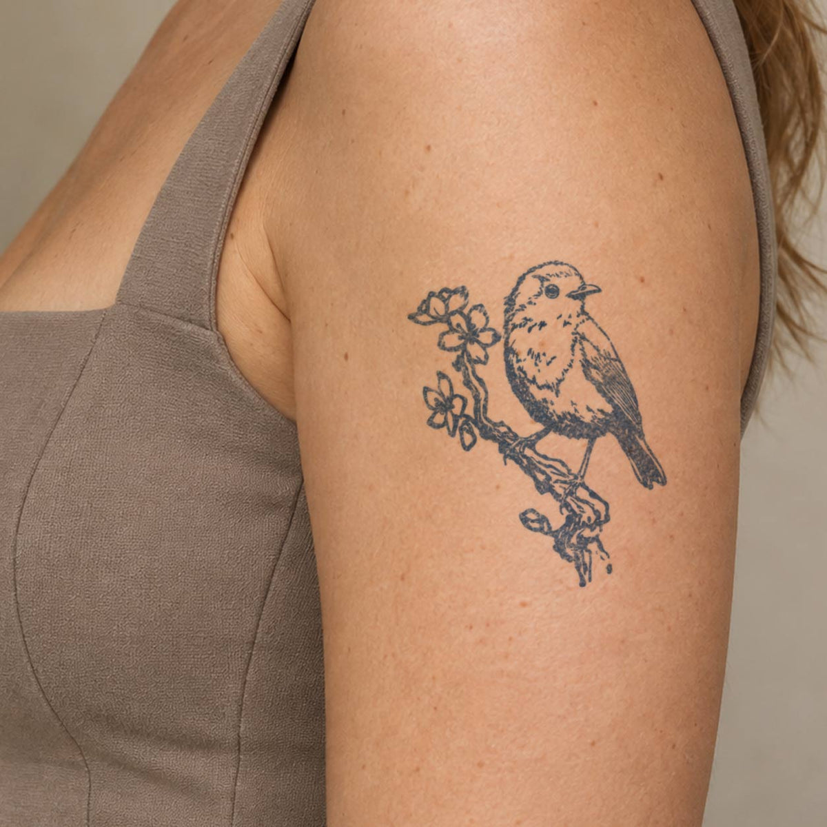 Bird temporary  tattoo featuring a detailed songbird perched on a flowering branch in blue-black ink on the upper arm.