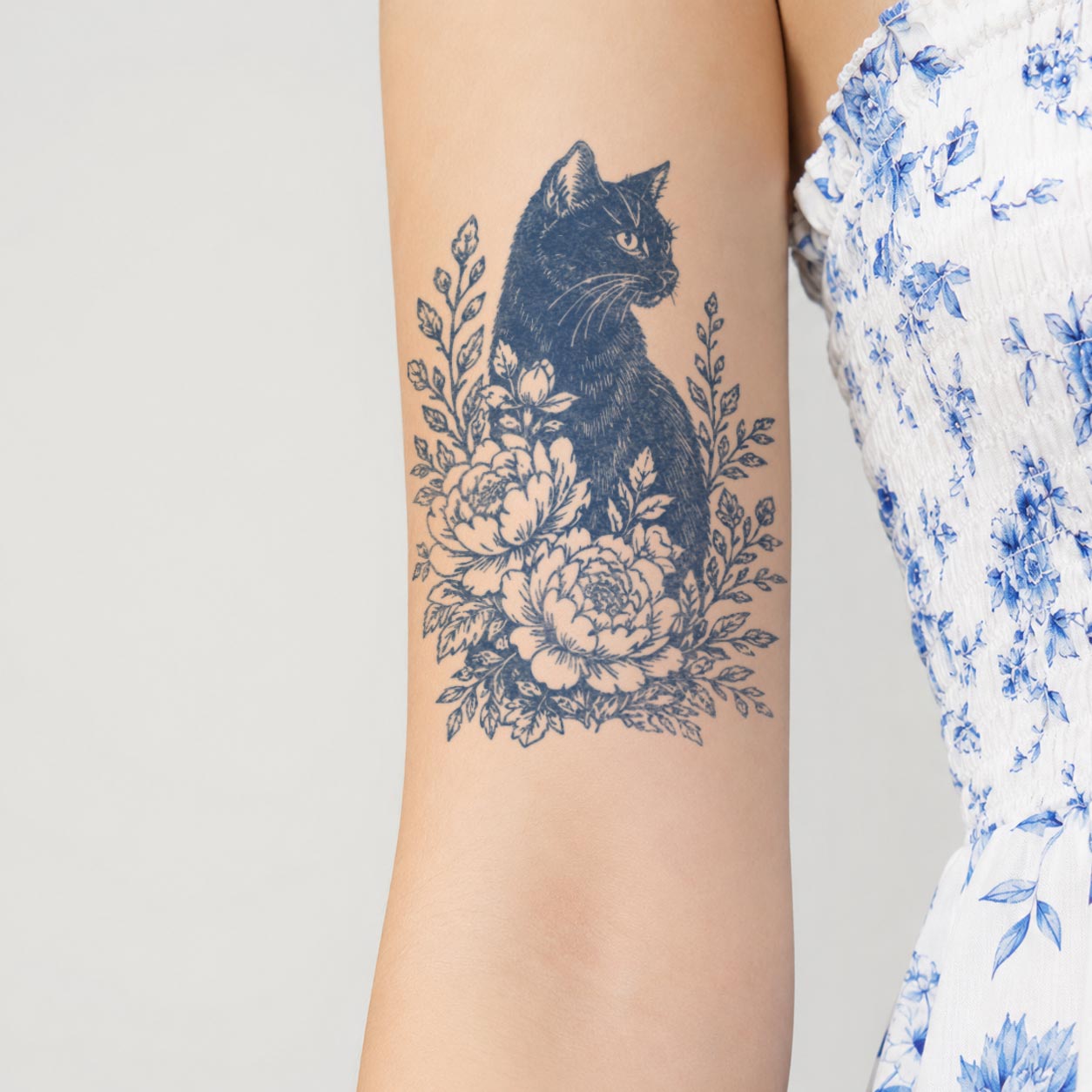Temporary arm tattoos featuring a seated black cat surrounded by large blossoms, leaves, and botanical branches.

