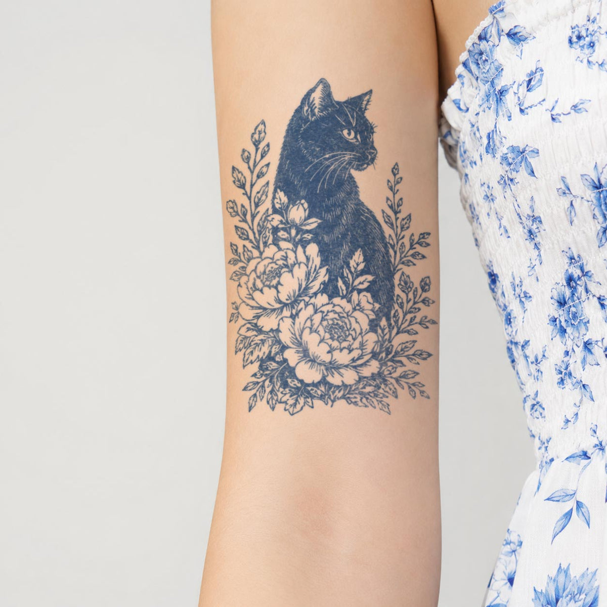 Temporary arm tattoos featuring a seated black cat surrounded by large blossoms, leaves, and botanical branches.
