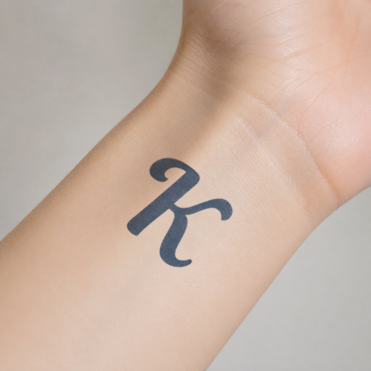 Bold black K abstract symbol temporary tattoo displayed on the inner wrist, with smooth curled ends and a clean minimalist look.