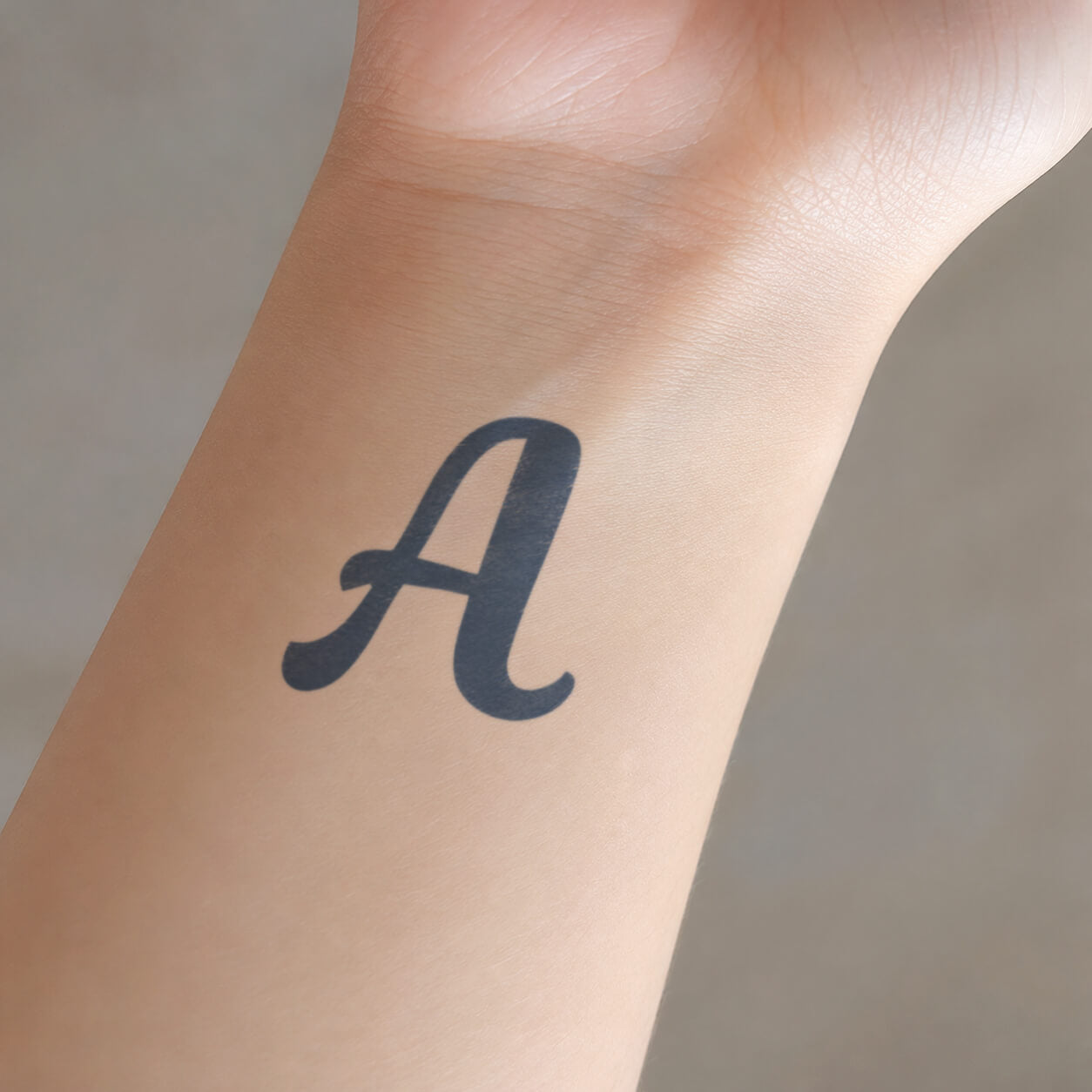 Bold black letter A temporary tattoo displayed on the inner wrist, featuring a smooth serif-inspired shape for a clean personalized initial look.
