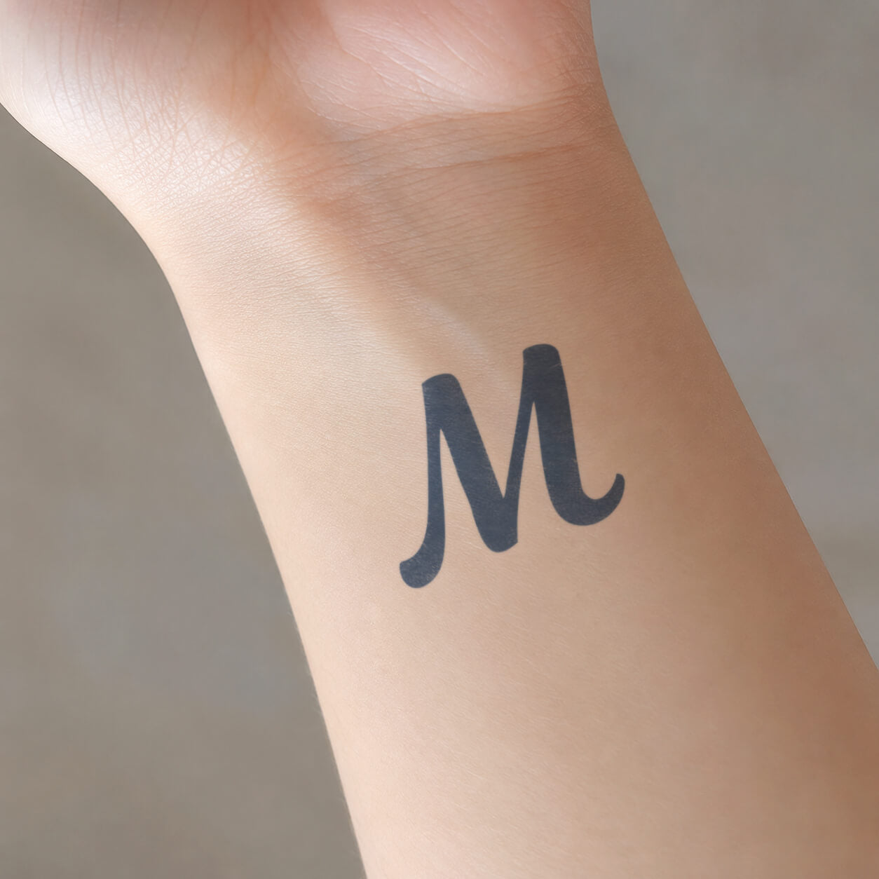 Bold black letter M design from custom temporary tattoos, shown on the inner wrist with a clean, simple typographic style.