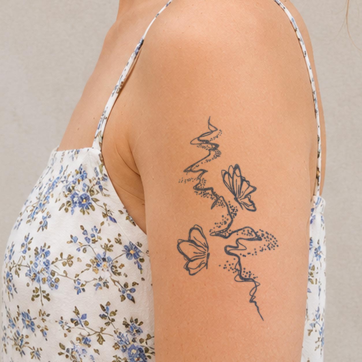 Temporary shoulder tattoos featuring two line-art butterflies moving along a dotted, winding trail.
