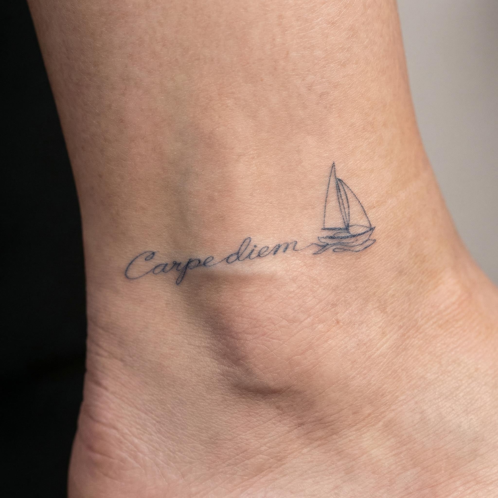 Minimal sailboat quote tattoo worn on the wrist with delicate script lettering