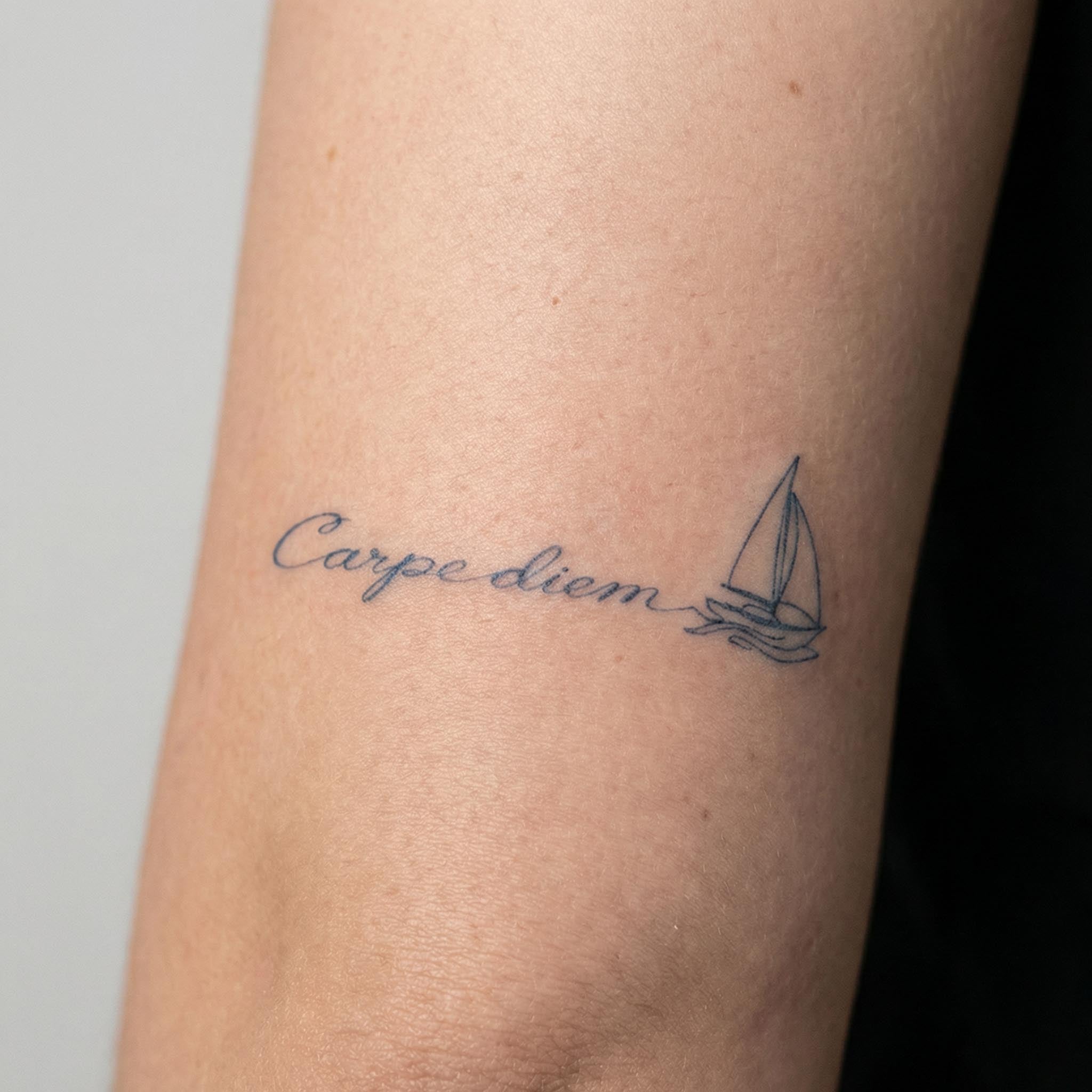 Minimal sailboat quote tattoo worn on the wrist with delicate script lettering