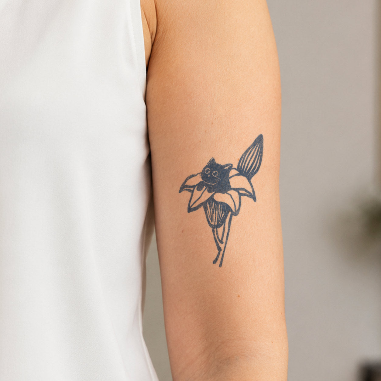 Temporary arm tattoos featuring a small black cat nestled inside a large blooming flower with long petals.
