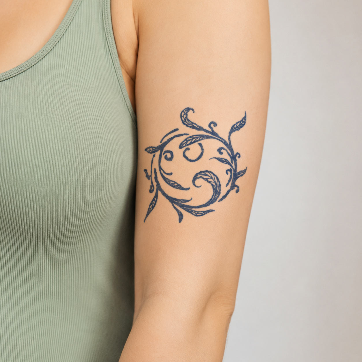 Botanical temporary tattoo featuring a circular wreath of curling leafy vines with hand-drawn leaves on the upper arm.