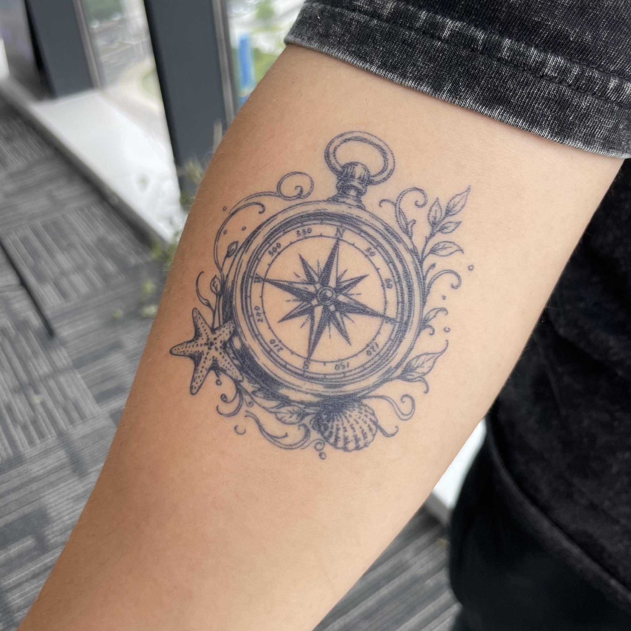 Compass semi-permanent tattoo with ocean-inspired details on forearm