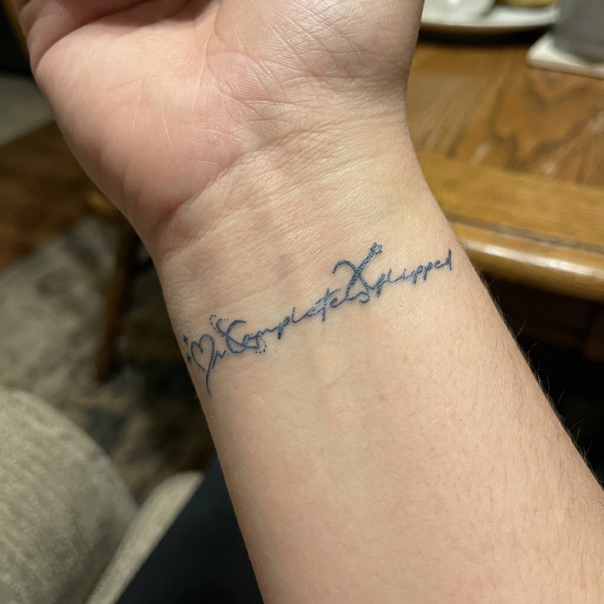 Minimal word fake tattoo worn on the wrist with “Completely Flipped”.