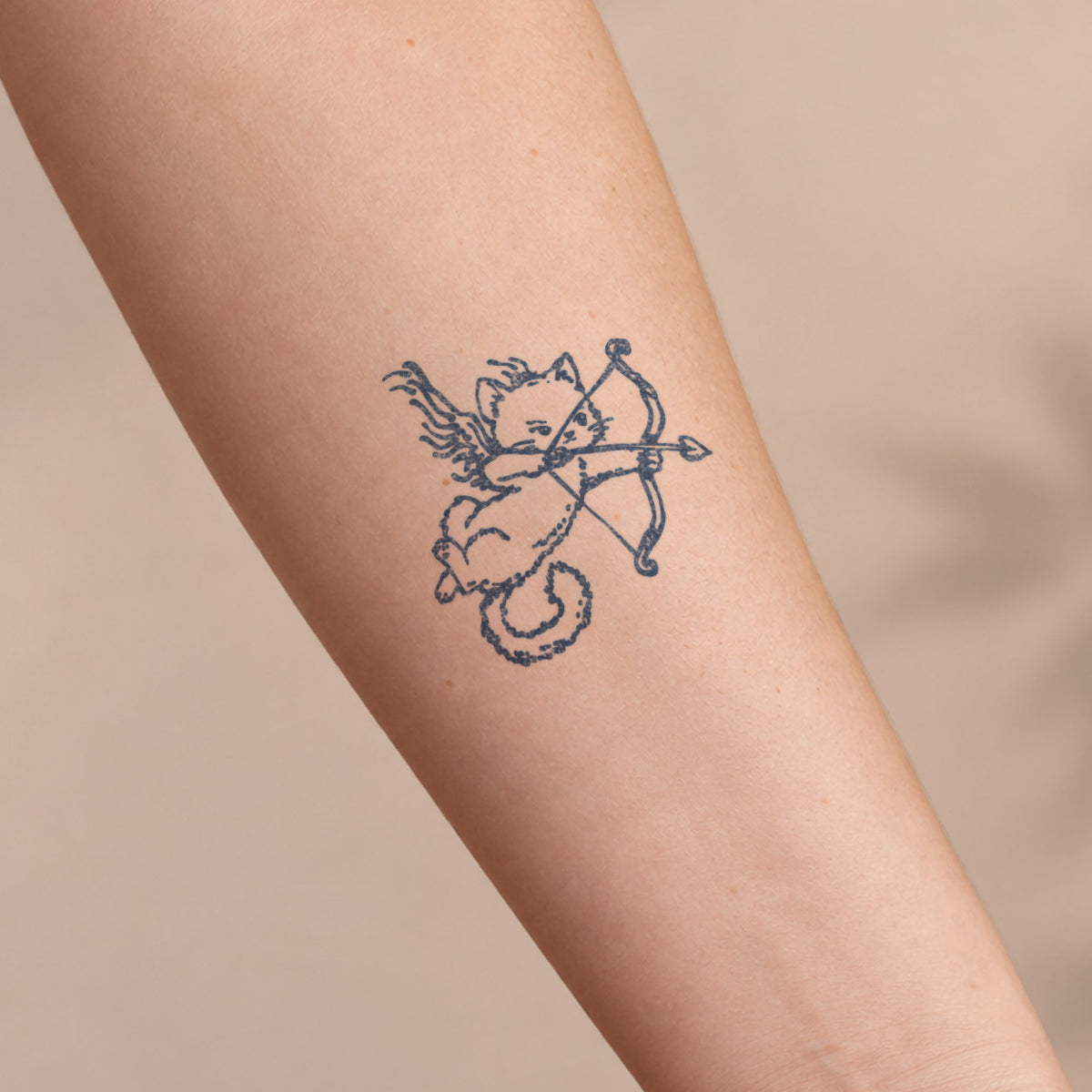 Aesthetic temporary tattoos featuring a cute winged cat Cupid holding a bow and arrow in blue-black line art on the forearm.