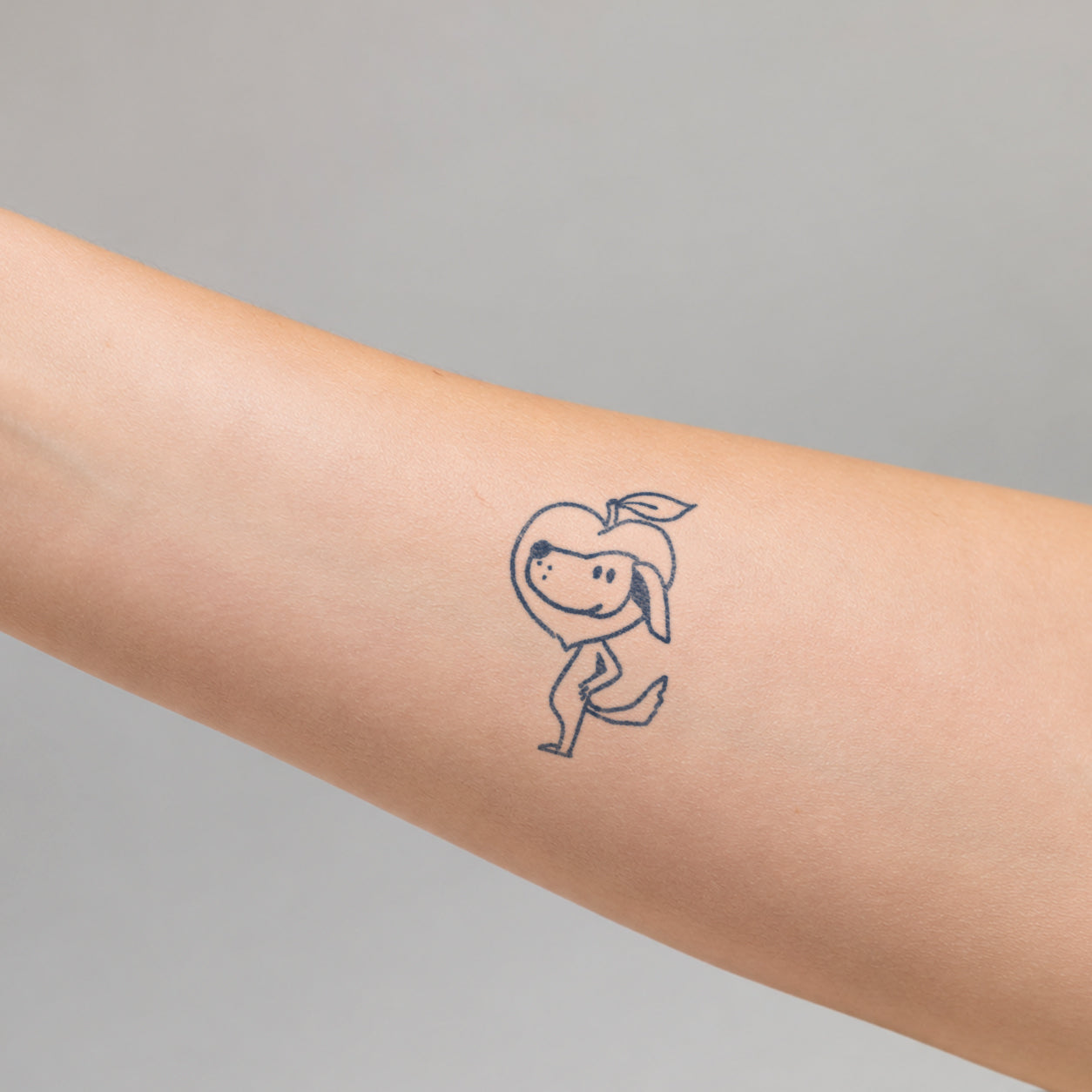 Playful minimalist tattoo featuring a cute smiling apple and character dog with a small leaf and simple cartoon details on the arm. This fun temporary tattoo design adds a cheerful and creative touch with a simple hand-drawn style.