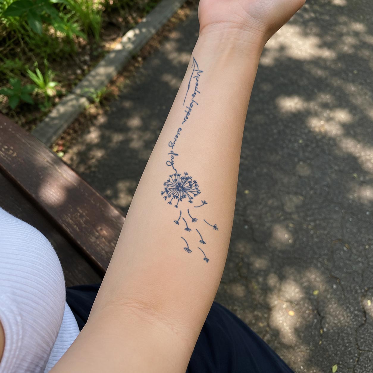 Flower temporary tattoo featuring a drifting dandelion with scattered seeds and a delicate handwritten quote along the inner forearm.