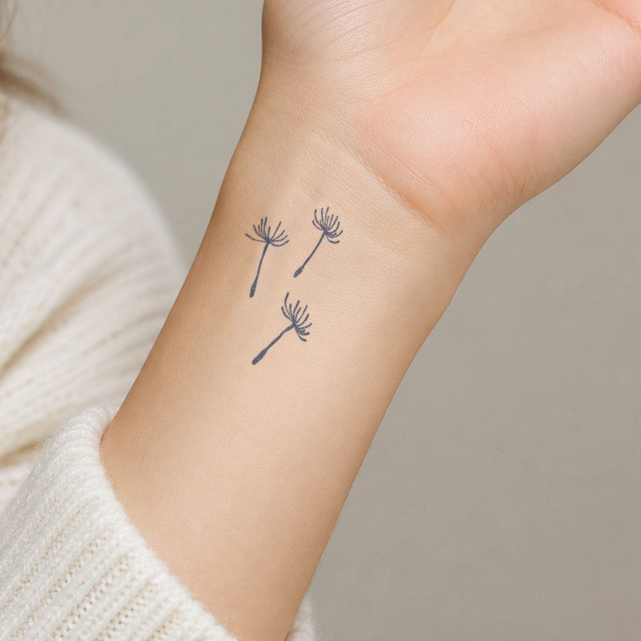 Minimal temporary tattoo design of three floating dandelion seeds, placed delicately on the inner wrist.