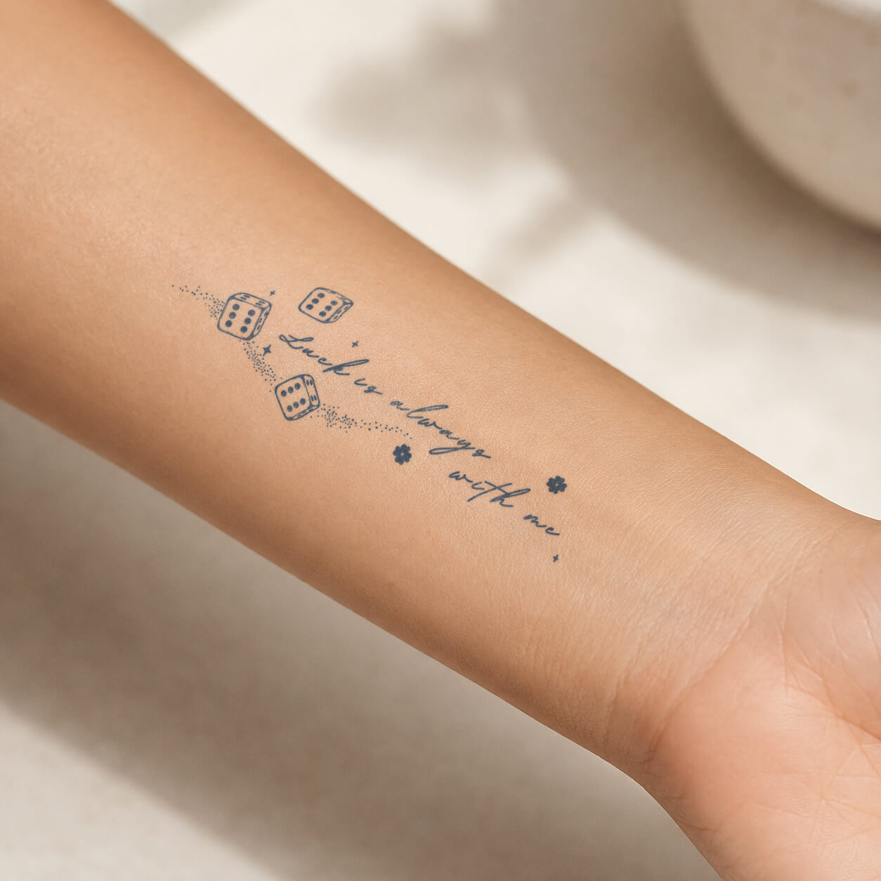 Fine-line dice and “Luck is always with me” quote shown as a waterproof temporary tattoo on the inner forearm, with dotted accents and tiny flowers.