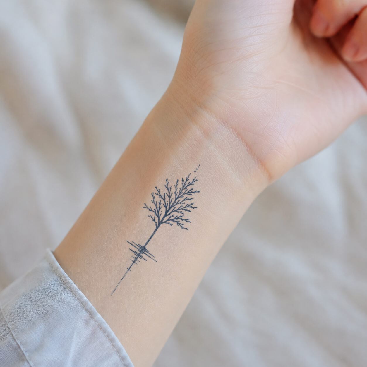 Delicate semi permanent tattoo featuring a fine-line tree and its mirrored reflection, displayed vertically along the inner wrist.