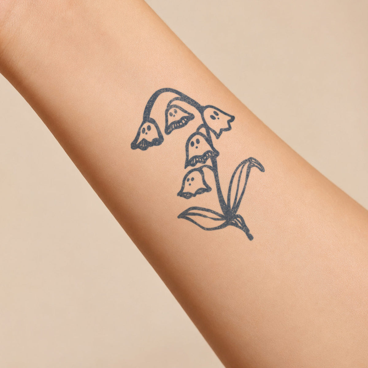 Temporary flower tattoos featuring whimsical bell-shaped flowers with cute ghost-like faces in blue-black ink on the forearm.