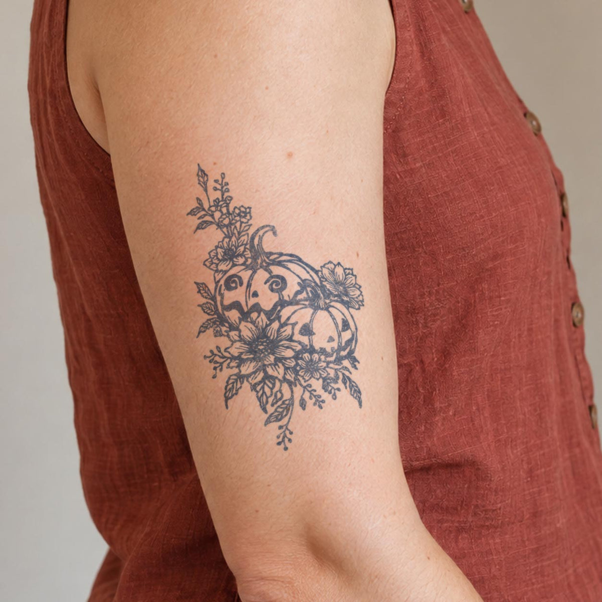 Floral temporary tattoos featuring two Halloween pumpkins surrounded by detailed flowers and leaves in blue-black ink on the upper arm.