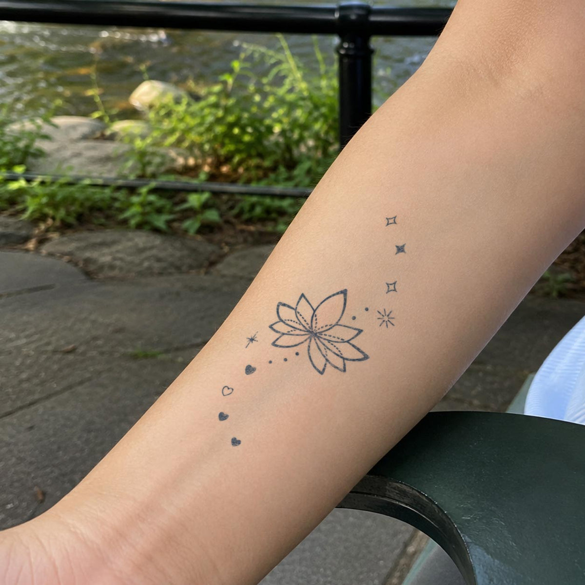 Temporary flower tattoos featuring a minimalist lotus surrounded by small stars and heart details in blue-black ink on the forearm.