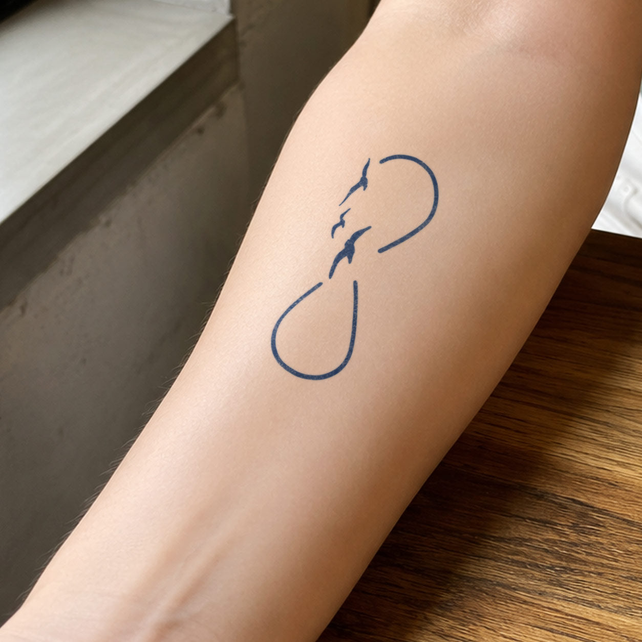 This temporary bird tattoo design features three small birds flying among infinity symbols and is tattooed on the inside of the forearm.
