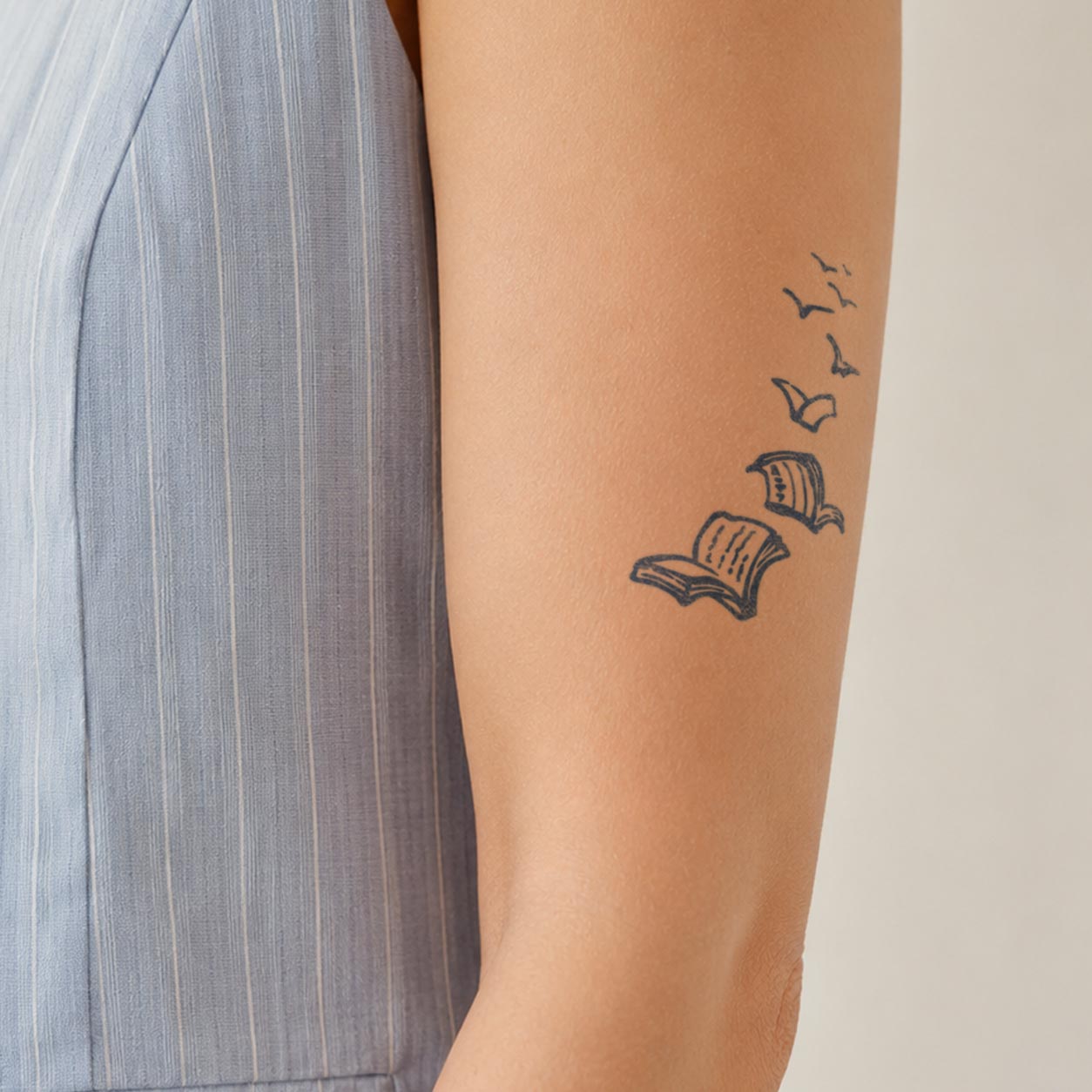 Temporary arm tattoos featuring two open books with loose pages transforming into flying birds.