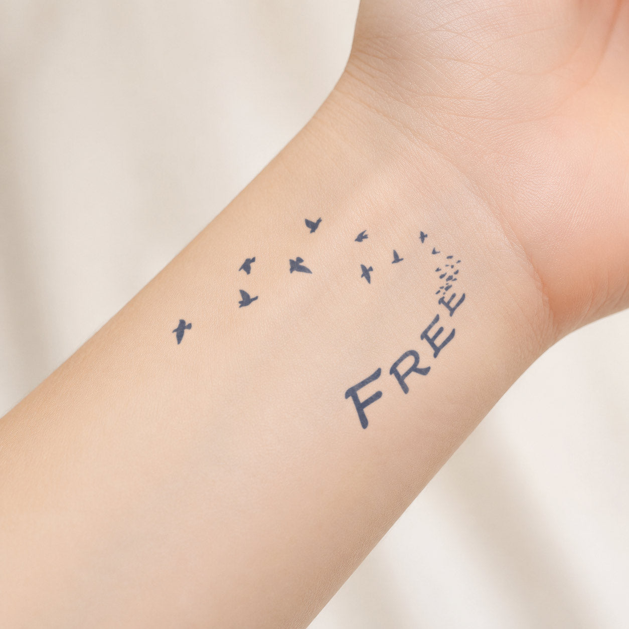 Semi-permanent tattoo design featuring the word “FREE” dissolving into a flock of flying birds on the inner wrist.