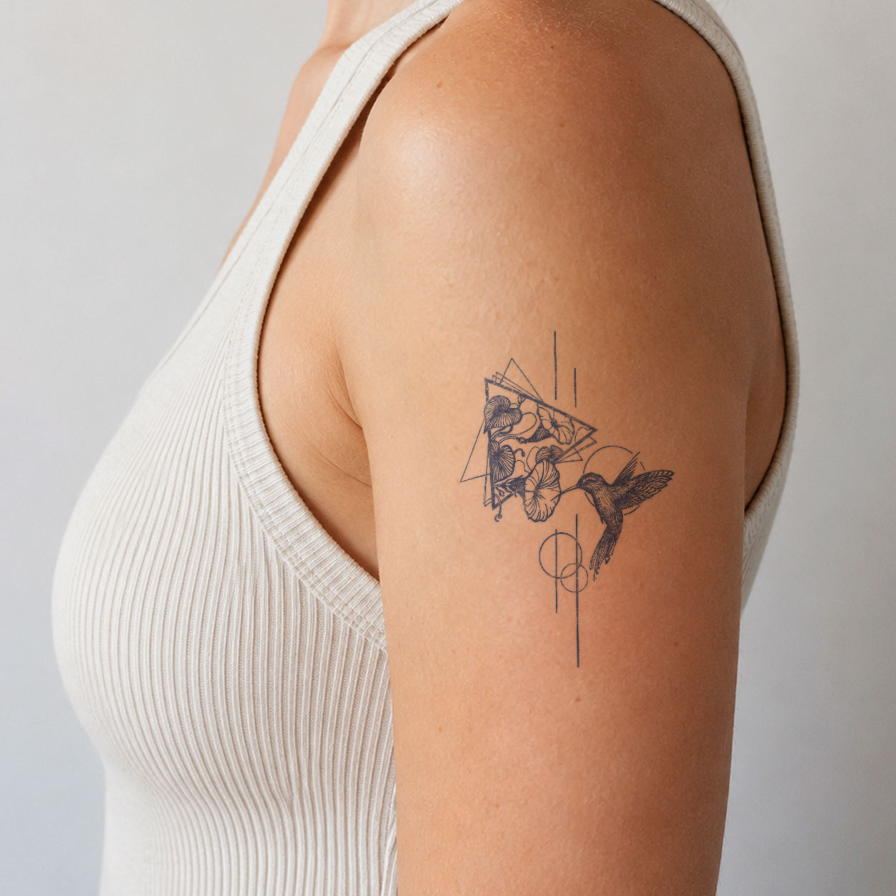 Fine-line semi-permanent tattoo featuring a hummingbird with floral details and delicate geometric accents on the upper arm.