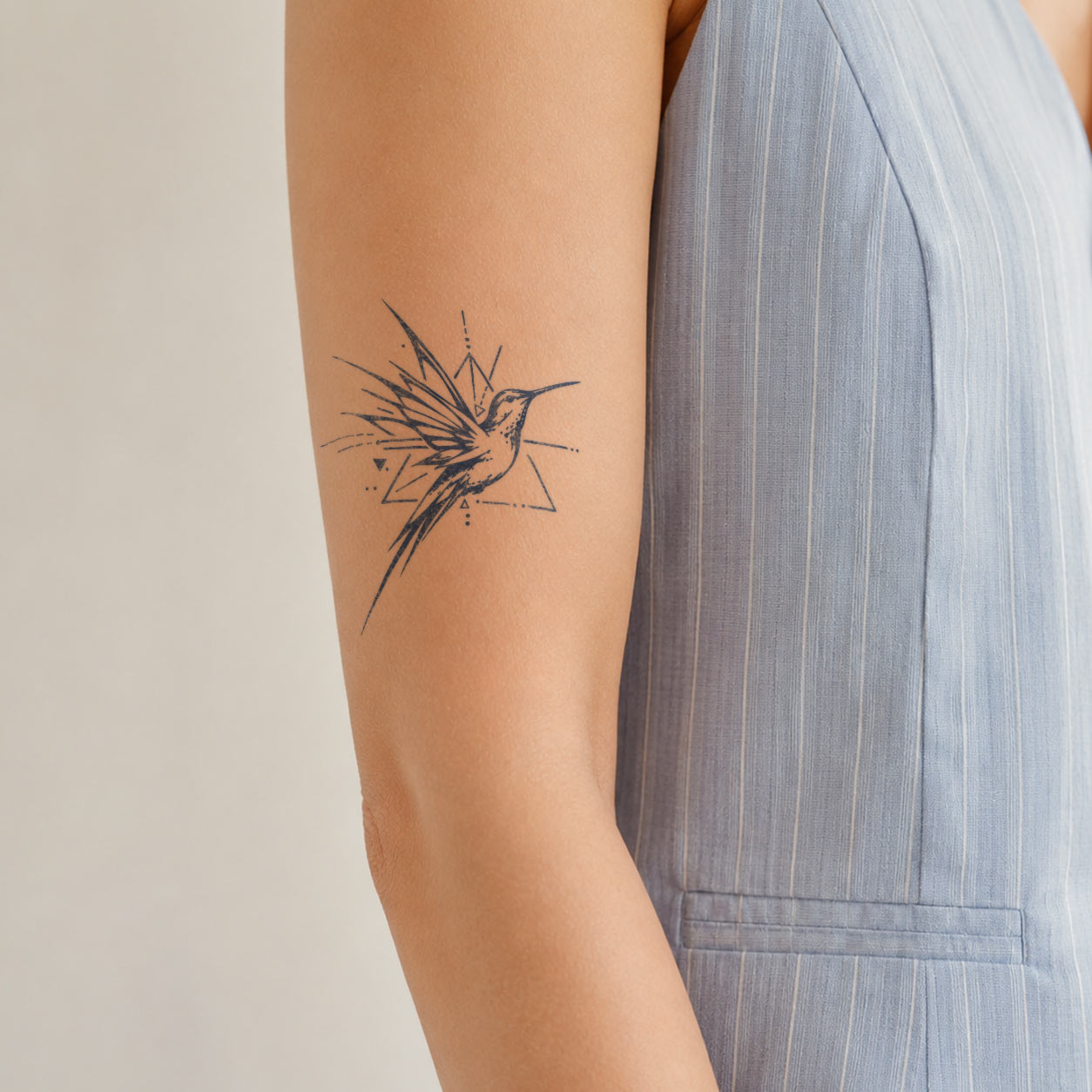 Fine-line semi-permanent tattoo featuring a hummingbird in flight with geometric accents on the upper arm.