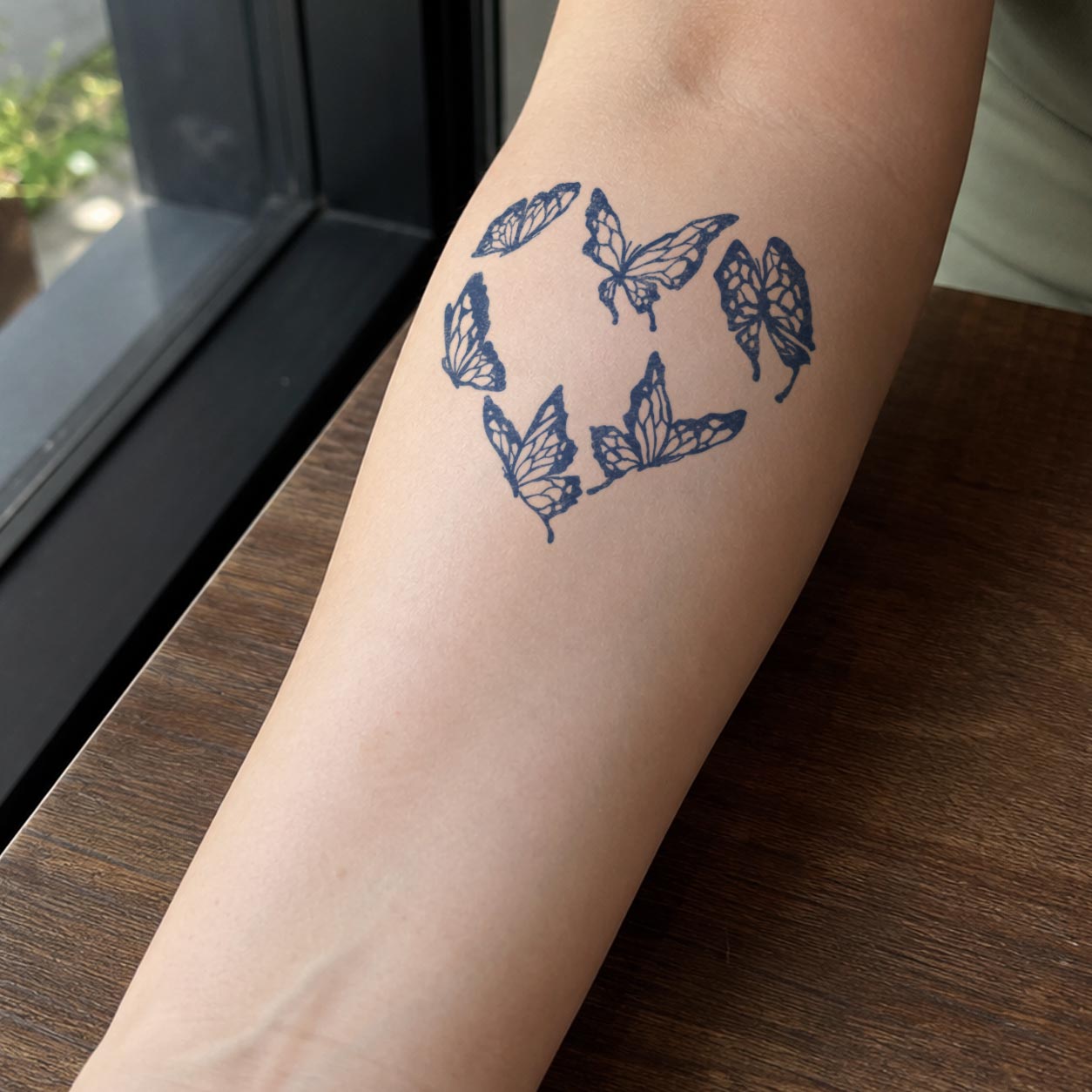 Butterfly temporary tattoo featuring multiple butterflies arranged into a soft heart-shaped outline on the inner forearm.