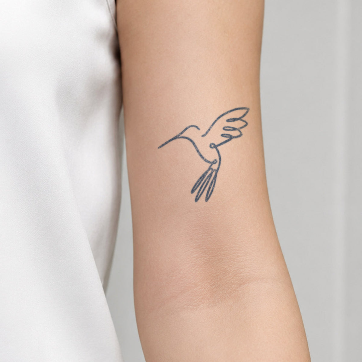 Temporary forearm tattoos featuring a delicate cursive word with an extended fine line in blue-black ink near the wrist.