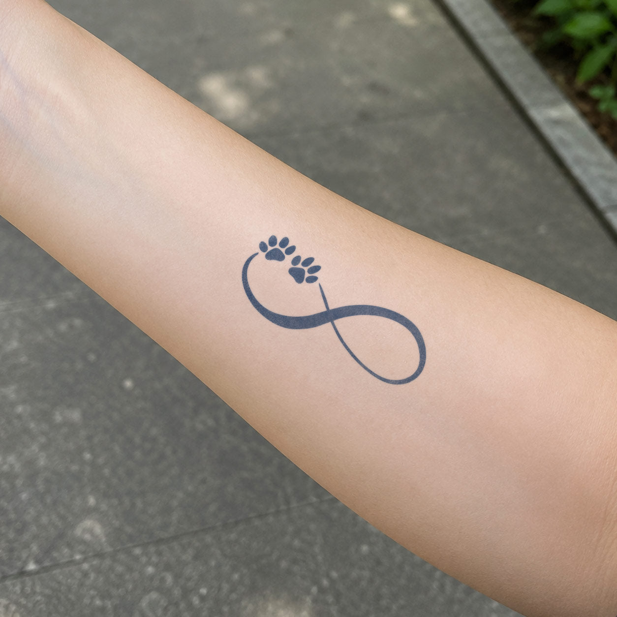 Temporary forearm tattoos featuring two paw prints placed along a flowing infinity symbol.