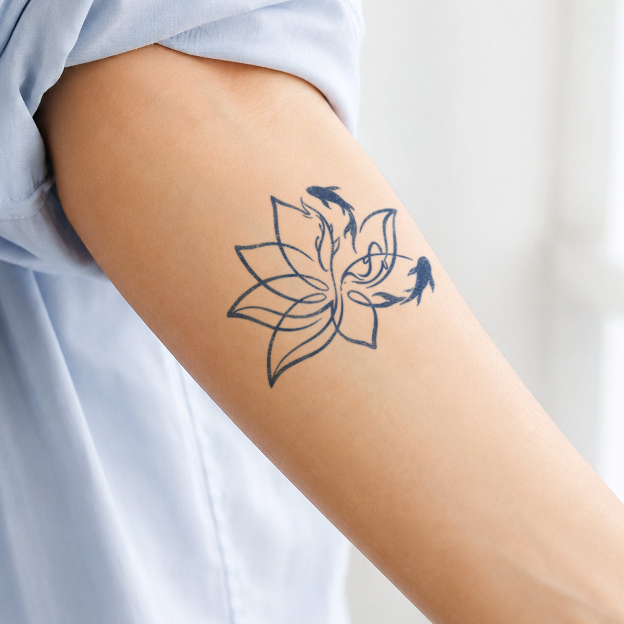 Temporary tattoo featuring three koi fish swimming around a large line-art lotus flower on the outer upper arm.
