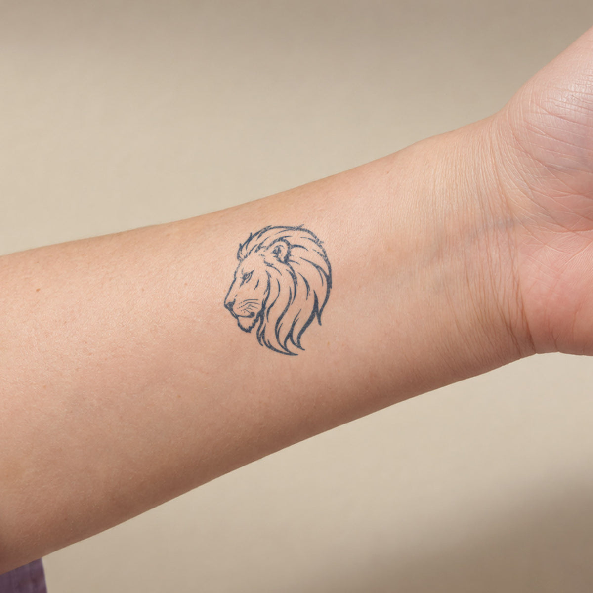 Realistic temporary tattoos featuring a minimalist lion head design in blue-black line art on the inner forearm.