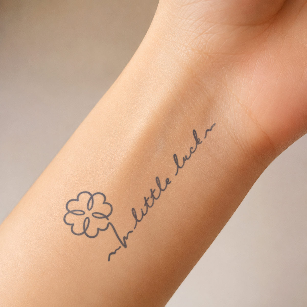 Semi-permanent tattoo featuring a four-leaf clover and “little luck” lettering, displayed on the inner wrist as a small lucky charm design.