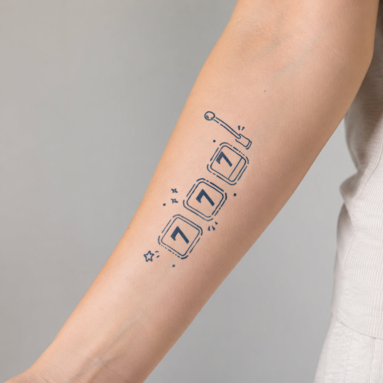 Minimal slot machine tattoo design featuring three game reels, a pull lever, and playful decorative details on the forearm. A fun temporary tattoo inspired by casino games, luck, and retro arcade style.