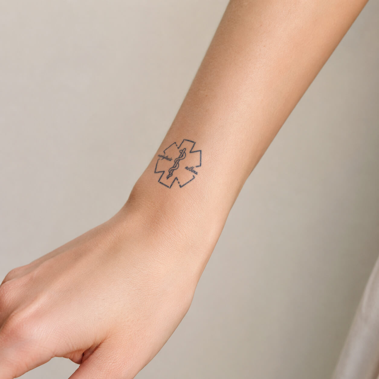 Small medical alert tattoo design featuring a healthcare cross symbol, a caduceus staff, and fine script details on the wrist. This minimalist temporary tattoo represents care, healing, and a connection to the medical field with a clean line art style.