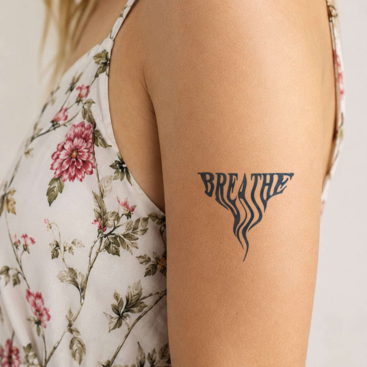 Close-up of a black Breathe word tattoo design with flowing curved lines extending downward, creating a calming minimalist style. This inspirational temporary tattoo features a simple wellness message and elegant lettering on the upper arm.