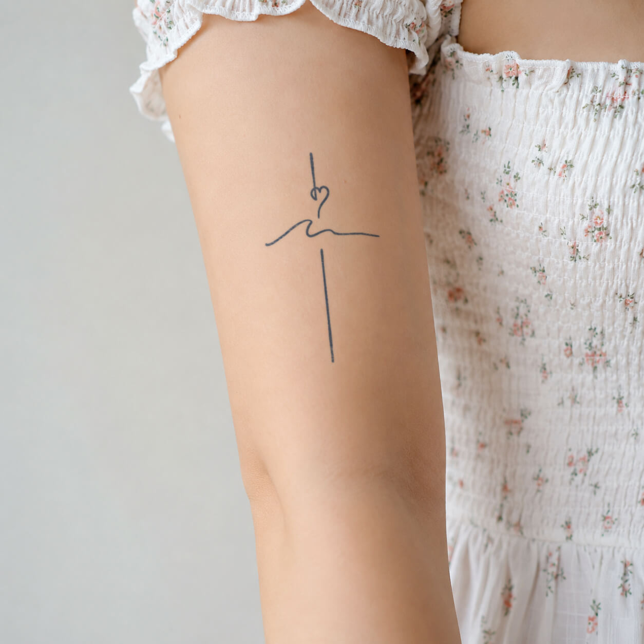 Minimal cross and heart line-art from our temporary tattoo designs, placed on the upper arm with a soft wave detail.