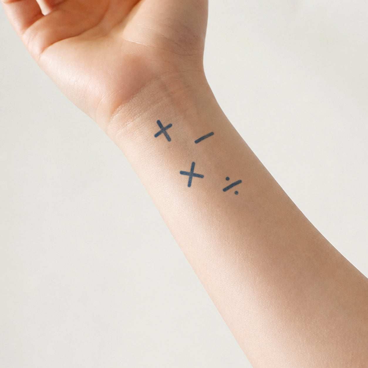 Minimal temporary tattoo featuring mathematical symbols including plus, minus, multiplication, and percentage signs on the inner wrist, creating a simple black ink design inspired by numbers and equations