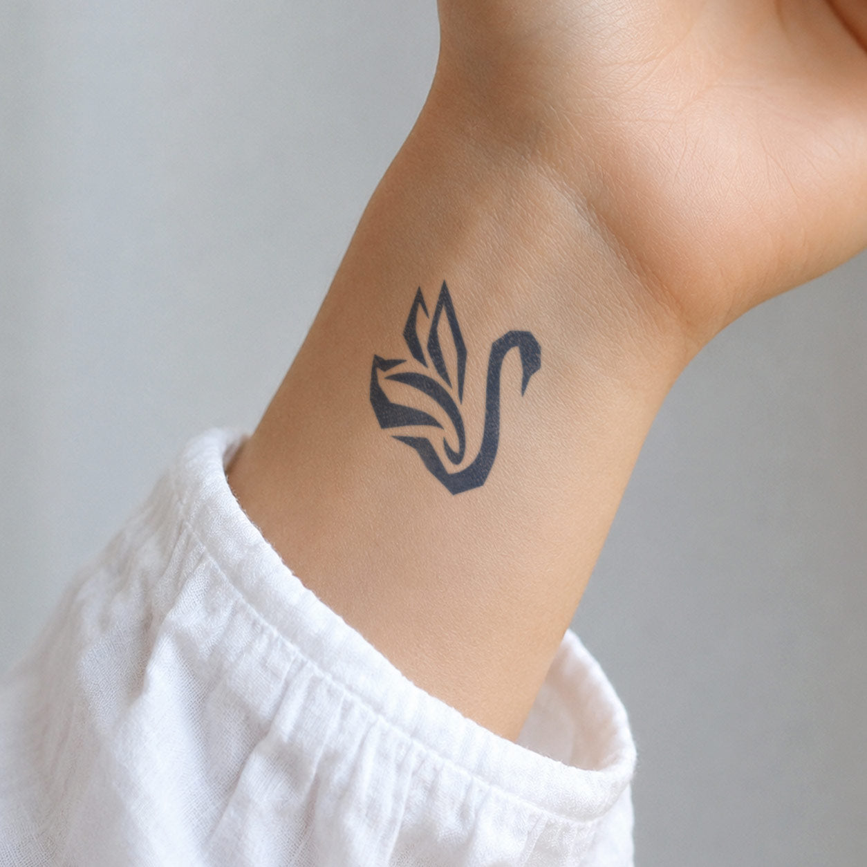 Temporary tattoo featuring a bold, stylized black swan on the inner wrist, designed with graceful curved lines and a clean black silhouette.