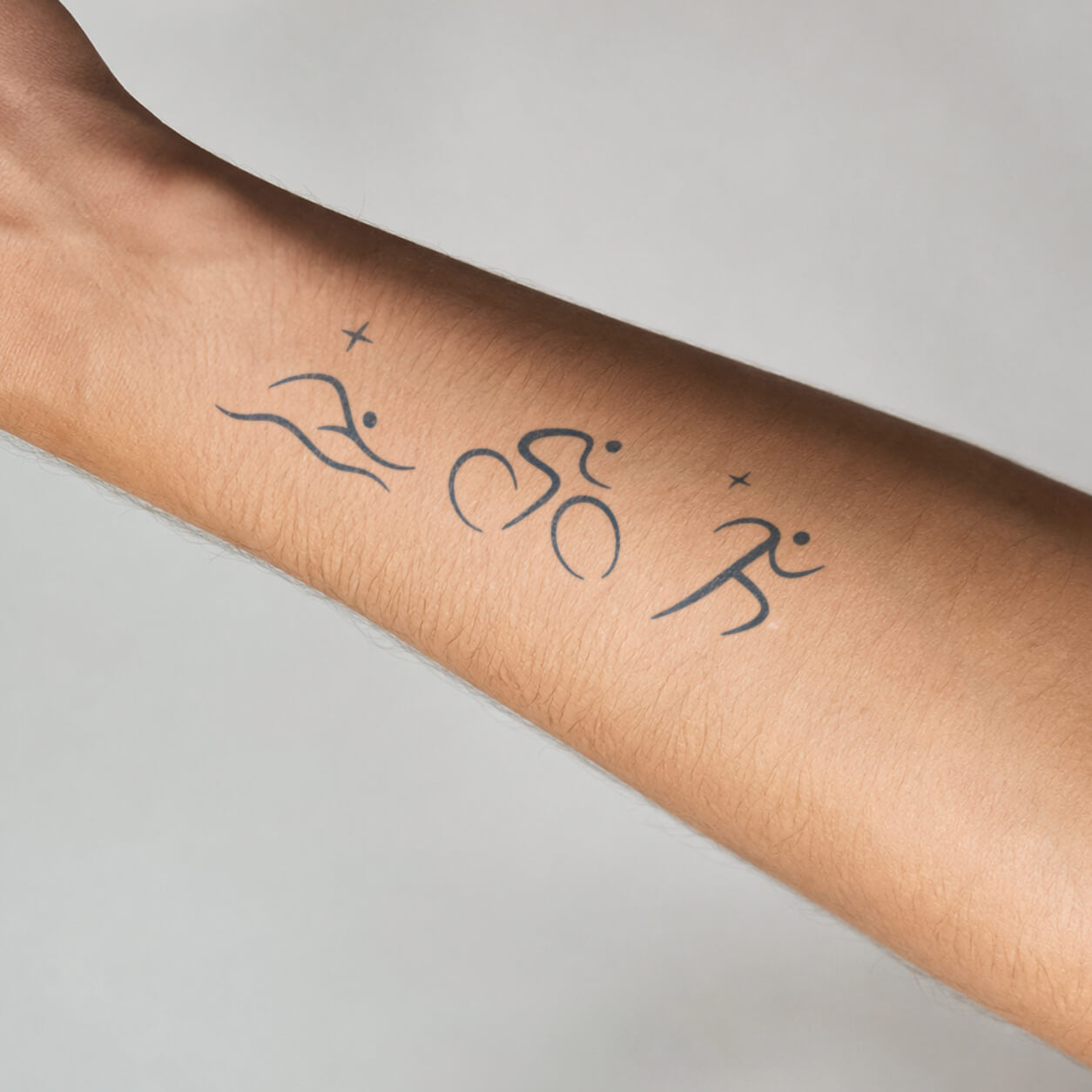 Minimal swim, bike and run line-art shown as  semi permanent tattoos on the inner forearm, with small star accents for a sporty look.