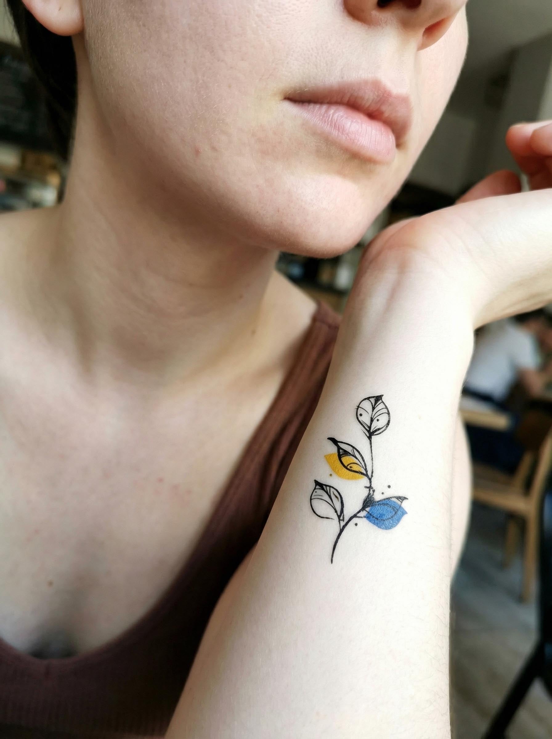 Branch tattoos applied on upper arm with watercolor fox and butterfly designs